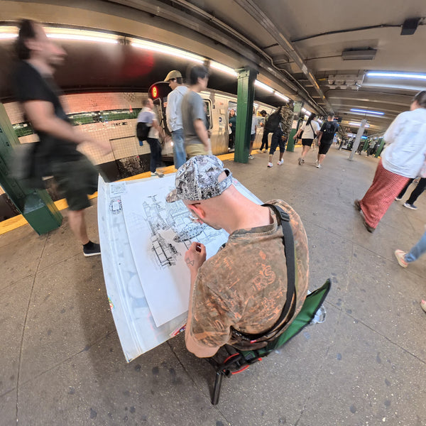 Heiner Radau drawing the large NYC artwork by hand on a New York subway platform with train and commuters passing by.