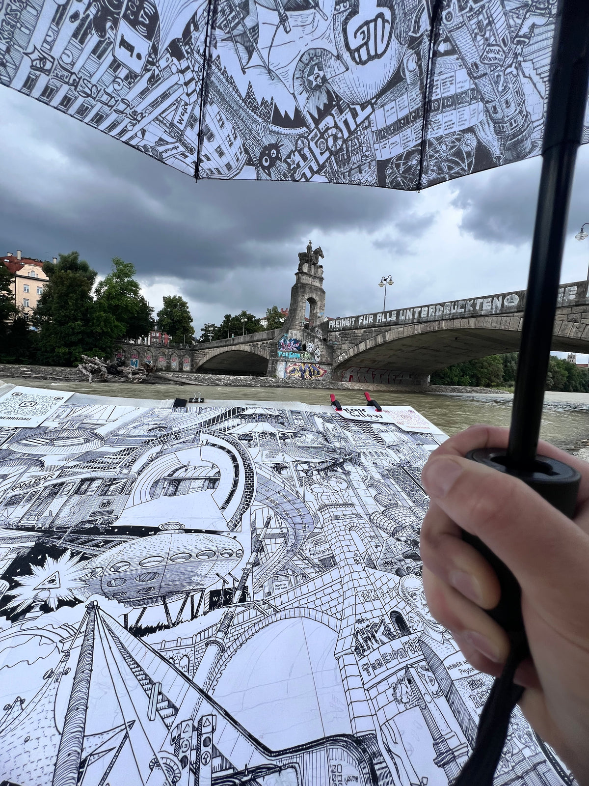 POV-Aufnahme: Heiner Radau zeichnet die Wittelsbacherbruecke aus der First-Person-Perspektive — Muenchener Isar-Bruecke in feiner Tusche-Linienfuehrung.