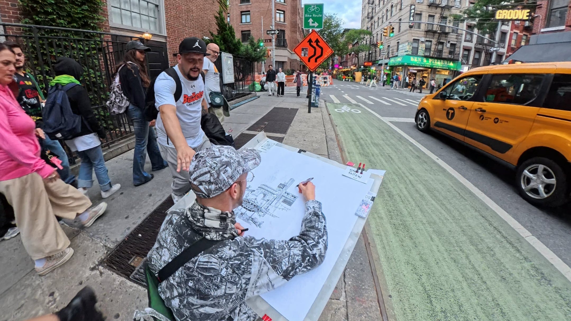 Artist painting a large canvas on a city street with pedestrians and a taxi in the background.