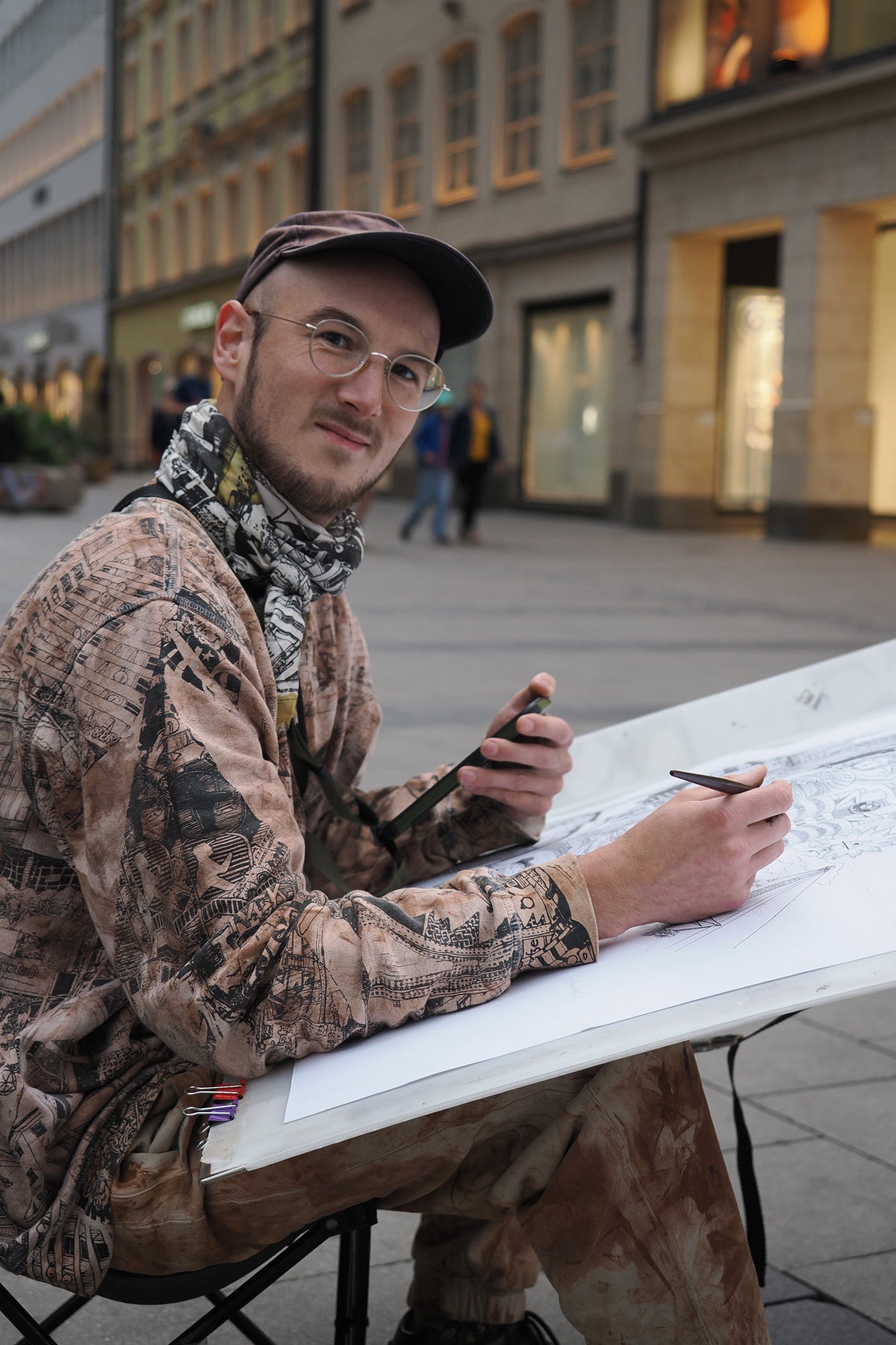 Heiner Radau bei der Arbeit am Zeichenbrett — das detailreiche Muenchen-Stadtkunstwerk entsteht live vor Ort mit Tinte und Feder.
