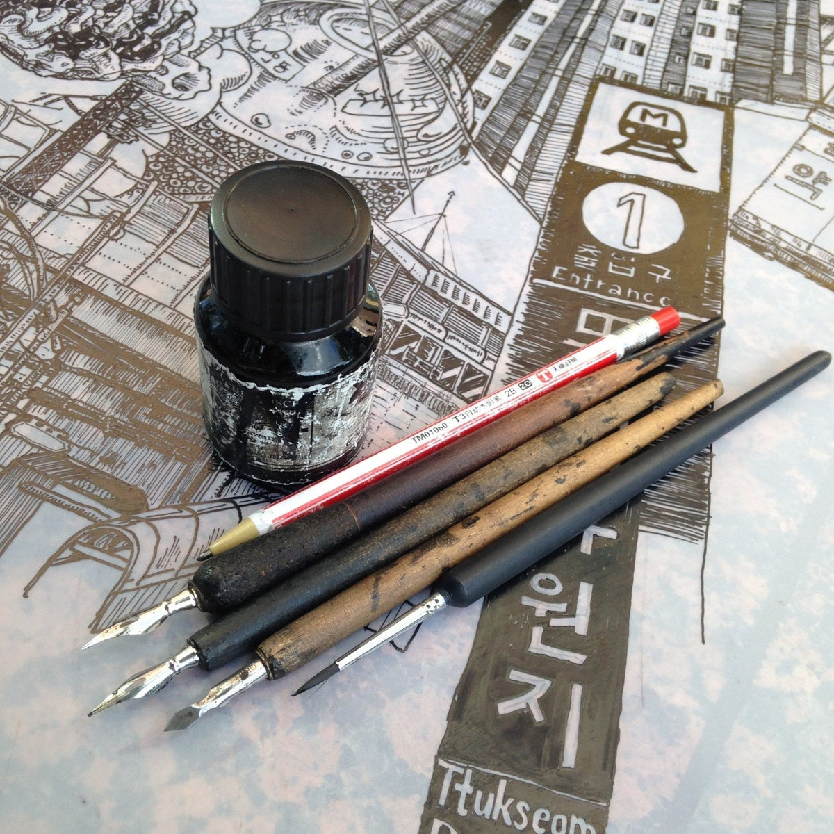Ink bottle, dip pens and pencil on a detailed ink drawing.